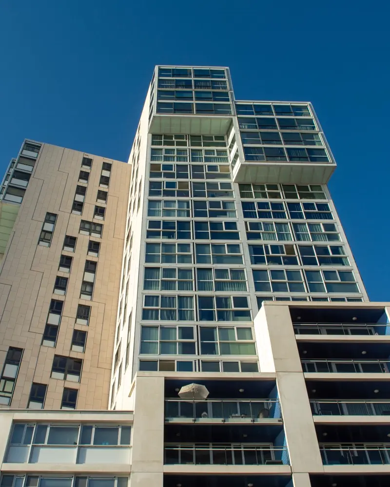 Torre residencial moderna com varandas envidraçadas, vista de baixo, ao lado de um bloco mais baixo.