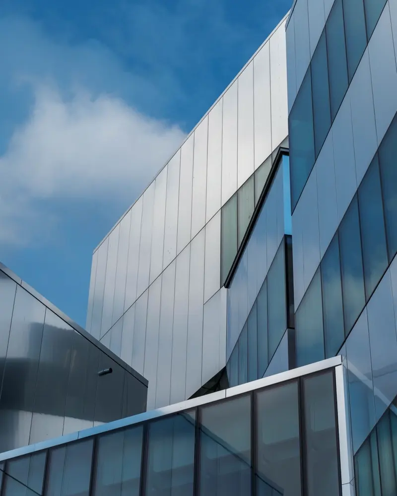 Fachada de vidro e painel metálico de um edifício contemporâneo, vista de baixo contra o céu.